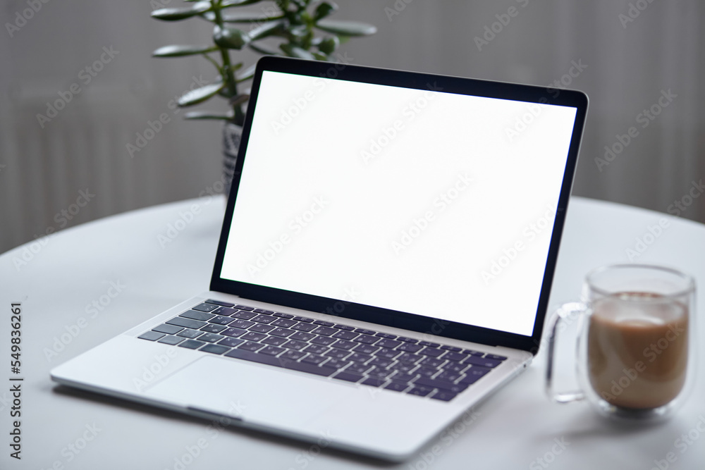 Fototapeta premium Close up laptop screen mockup on table with coffee cup and houseplant at home, no people
