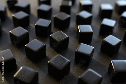Black blocks on a dark background. Scattered cubes. Abstraction, field blur. Simplicity and elegance. Solidity, shine.
