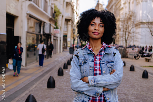 Fototapeta young black haitian woman looks at the camera with crossed arms, urban look and very confident