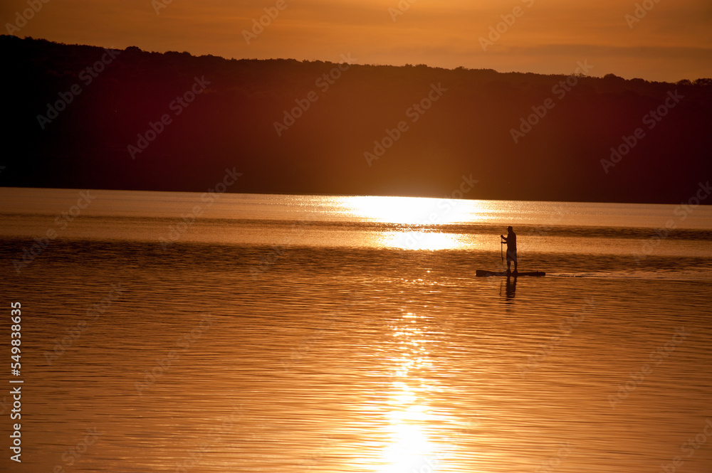 the silhouette of a man on a surfboard in the rays of the setting sun on the Ternopil pond