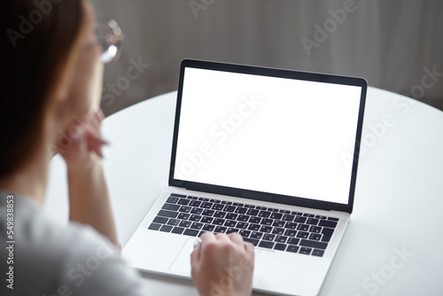 Mockup white screen laptop woman using computer while sitting at table at home, back view