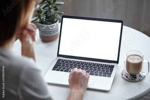 Mockup white screen laptop woman using computer while sitting at table at home, back view photo