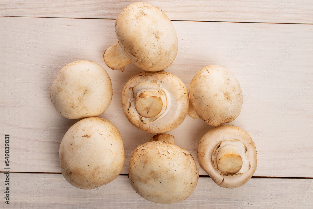 Several whole organic fresh mouth-watering champignon mushrooms, on a table made of natural wood, top view.