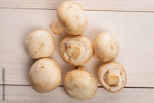 Several whole organic fresh mouth-watering champignon mushrooms, on a table made of natural wood, top view.
