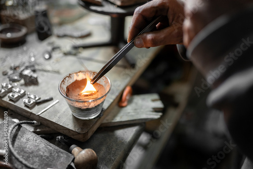 A craftsman jeweler is pouring some melted silver in a mold to make an unique piece