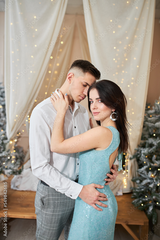 pretty couple in love kissing in christmas eve near tree with gifts at home in december.