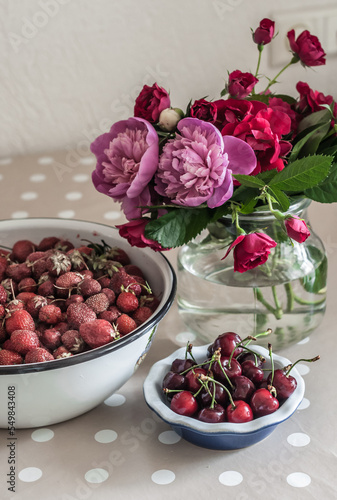 Strawberries  cherry in a ceramic plate and a bouquet of peonies.