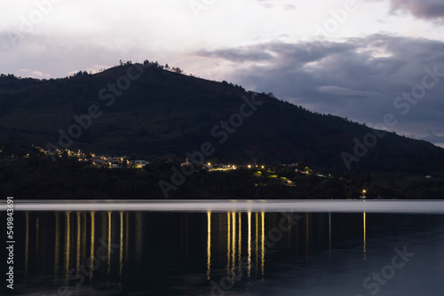 Beautiful Colombian Gachala town landscape with night light refflected on guavio reservoir lake and a big mountain silhouette on violet sunset photo