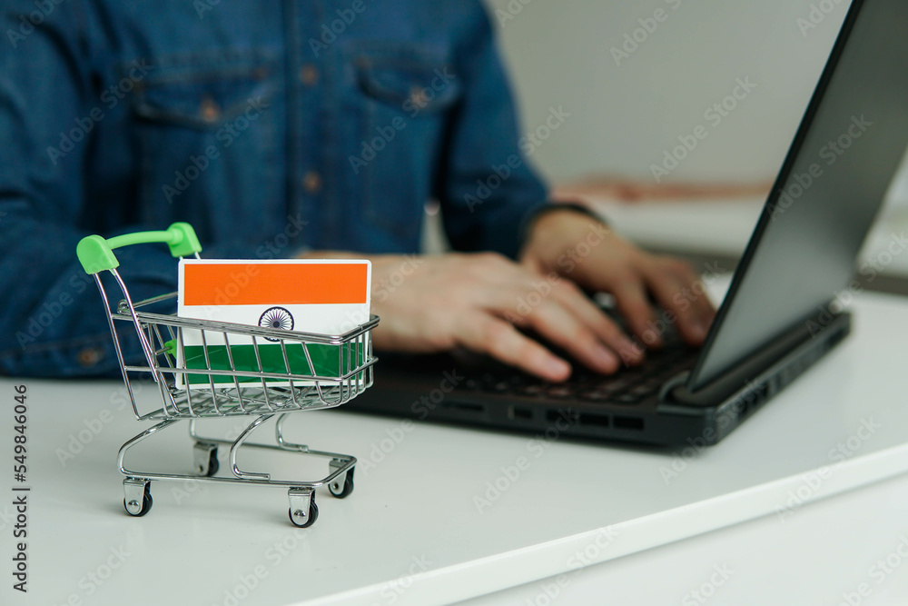 Small shopping cart with Indian Flag on the table. Man using laptop for shopping online.