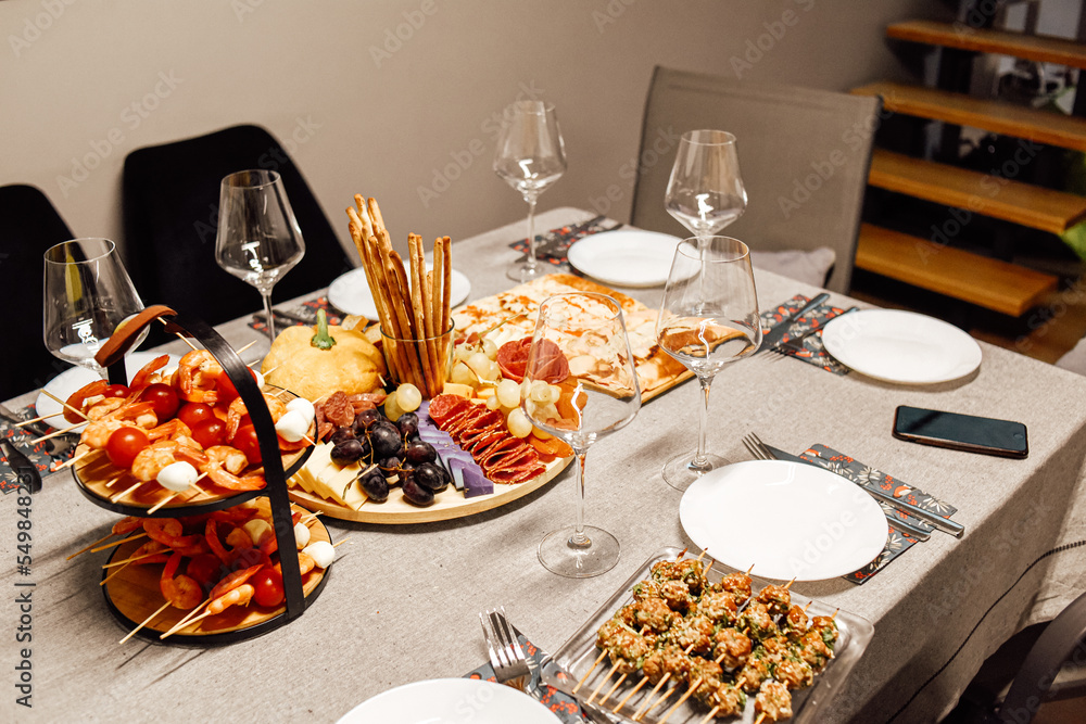 Cheese platter, cheese board meat and board. Vegetables and fruits with cheese and chocolate, prosciutto and salami with bread. Table with wine glasses, shrimp dinner.