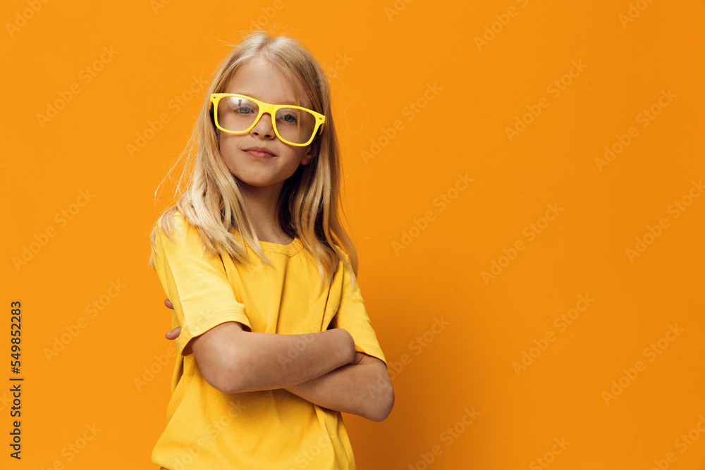 a serious concentrated girl in yellow glasses for vision stands with her arms folded on her chest. Horizontal photo on a yellow background with empty space for an advertising layout a serious concentrated girl in yellow glasses for vision stands with her arms folded on her chest. Horizontal photo on a yellow background with empty space for an advertising layout