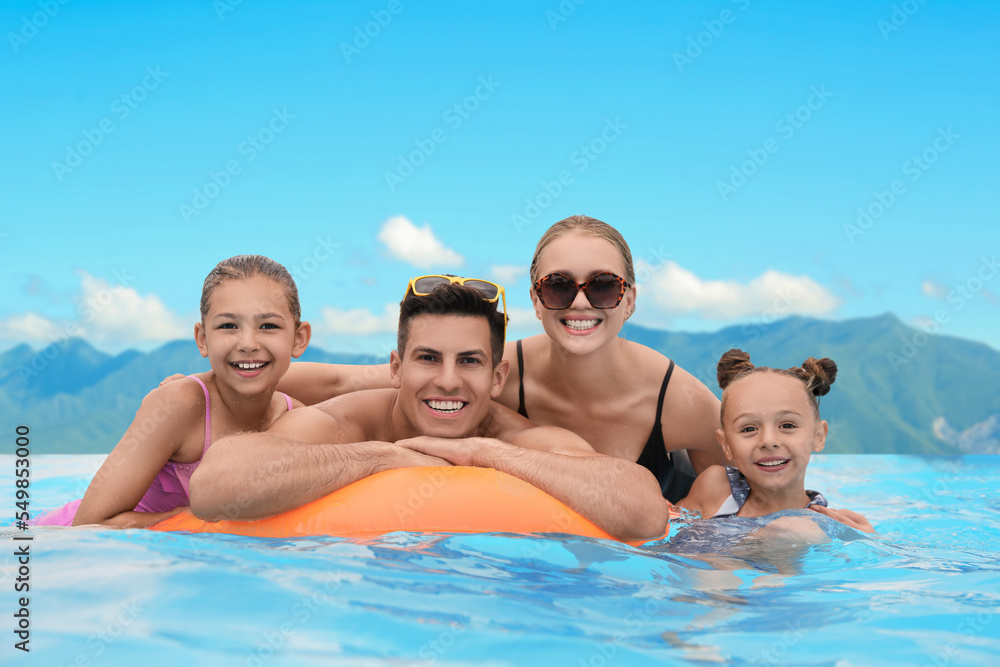 Happy family in outdoor swimming pool at luxury resort with beautiful view of mountains on sunny day Happy family in outdoor swimming pool at luxury resort with beautiful view of mountains on sunny day