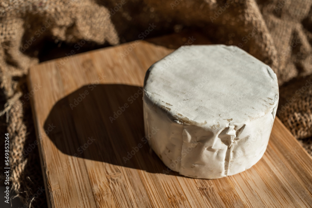 A composition of a round cheese head with white mold on a bamboo board on a background of burlap. Aesthetic serving of food A composition of a round cheese head with white mold on a bamboo board on a background of burlap. Aesthetic serving of food