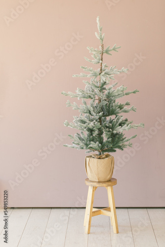 Small christmas tree sitting on top of stool in a minimal room