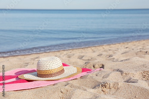 Beach towel and straw hat on sand near sea, space for text