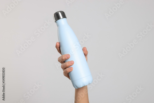 Woman holding thermo bottle of drink on light background, closeup