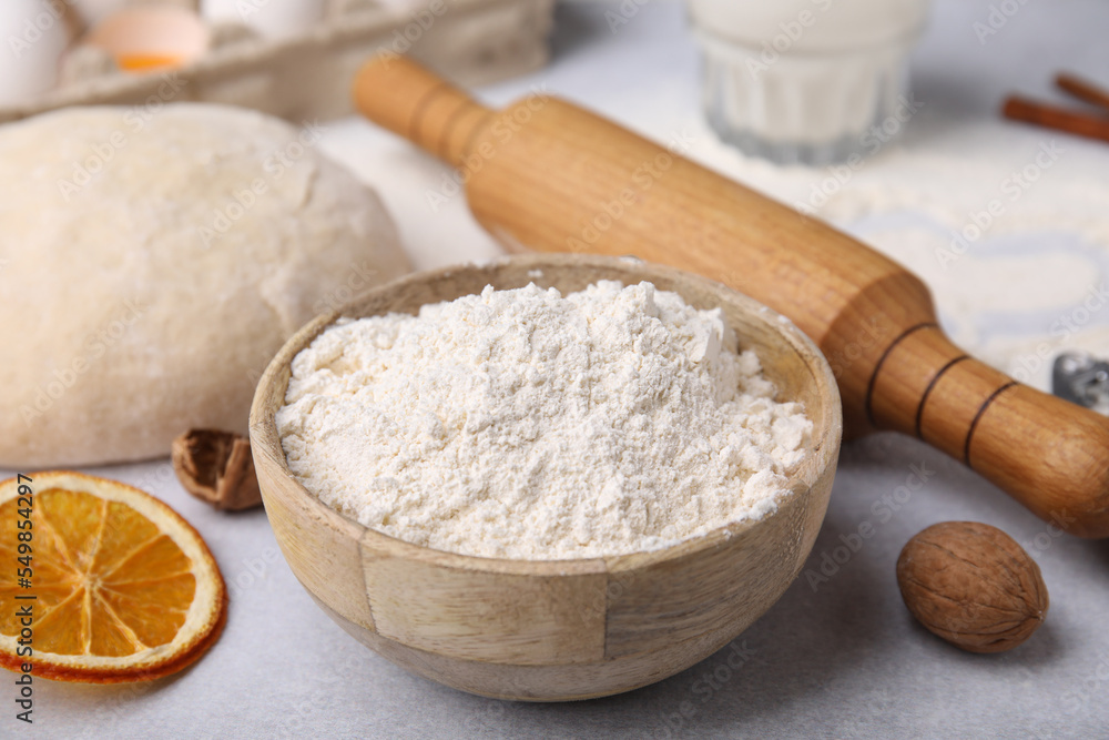 Bowl of flour, rolling pin and ingredients on white table