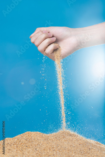 Hand releasing dropping sand. Fine Sand flowing pouring through fingers against blue background. Summer beach holiday vacation and time passing concept. Isolated high speed shutter