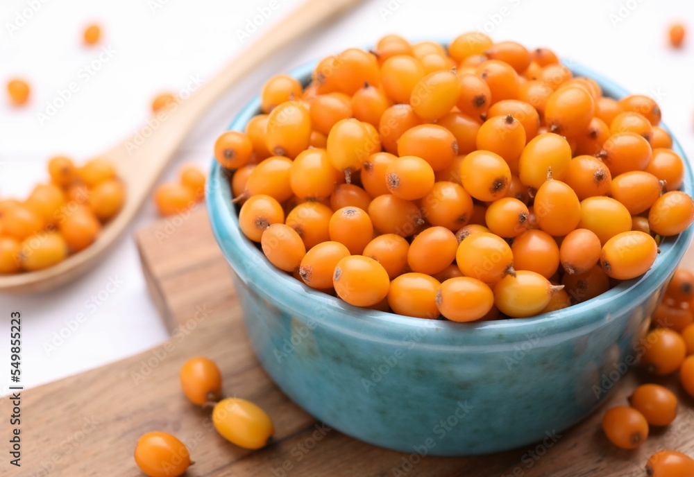 Bowl with fresh ripe sea buckthorn berries on wooden board, closeup