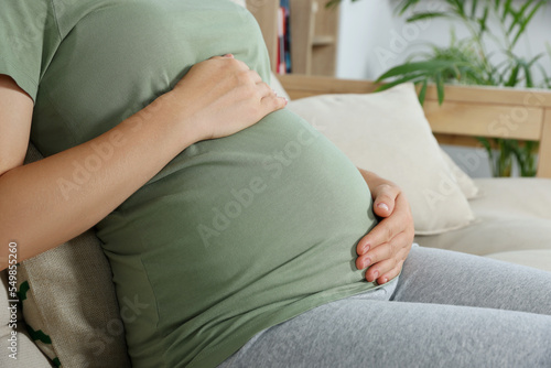 Pregnant woman touching belly in living room, closeup