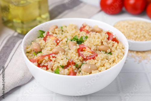 Delicious quinoa salad with tomatoes, beans and parsley served on white tiled table