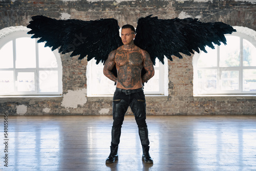  angel man with black wings, stand posing at camera. man fall from heaven, angel with muscular body gained freedom.  tattooed hot man. tattooed black angel. dark angel in leather