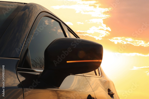Black modern car outdoors at sunset, closeup of side view mirror