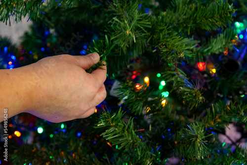 closeup of hand decorating artificial christmas tree placing christmas lights on green tree