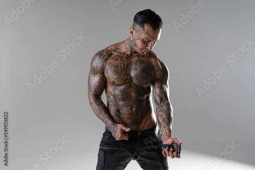 Handsome brutal man with tattoo holding belt and watching us. hot sportive guy in studio. bodybuilder. punisher