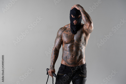 Muscular shirtless young man with whip in a mask.Brutal handsome man with tattooed body. Men tattoo casual fashion. Portrait of handsome male model. Muscular athletic sexy male with naked torso.