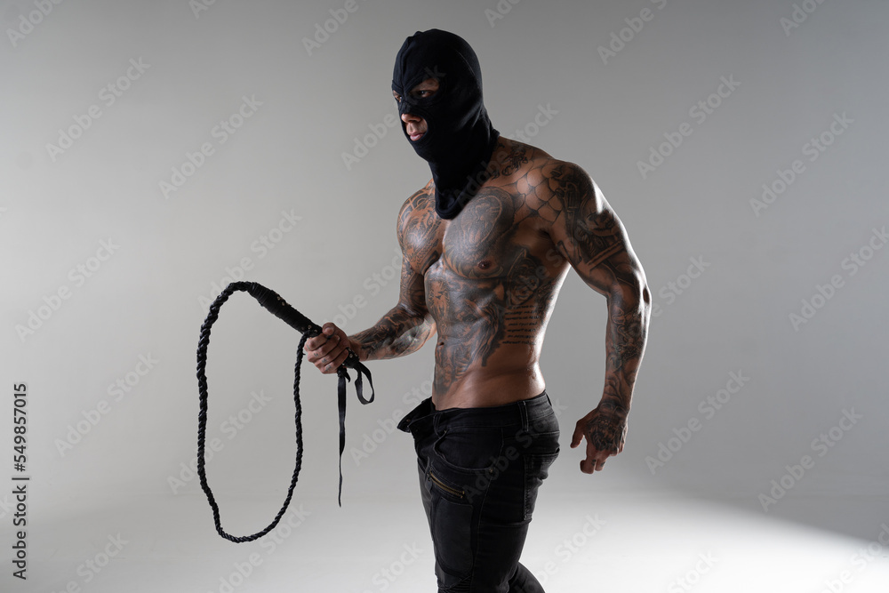 Muscular shirtless young man with whip in a mask.Brutal handsome