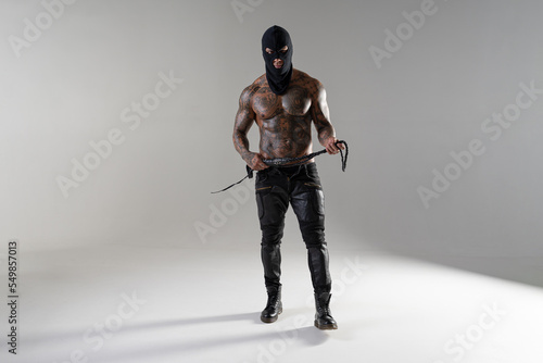 Muscular shirtless young man with whip in a mask.Brutal handsome man with tattooed body. Men tattoo casual fashion. Portrait of handsome male model. Muscular athletic sexy male with naked torso.