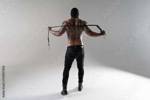Muscular shirtless young man with whip in a mask.Brutal handsome man with tattooed body. Men tattoo casual fashion. Portrait of handsome male model. Muscular athletic sexy male with naked torso.
