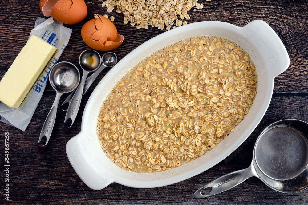Rolled Oats, Milk, and Other Baked Oatmeal Ingredients in an Oval Baking Dish: Uncooked oatmeal viewed from overhead and surrounded by ingredients Rolled Oats, Milk, and Other Baked Oatmeal Ingredients in an Oval Baking Dish: Uncooked oatmeal viewed from overhead and surrounded by ingredients