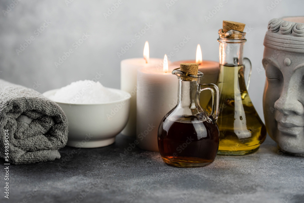 Spa massage relax composition setting. Natural essence oils, sea salt, towel, candles, Buddha head statue on gray background. Spa massage relax composition setting. Natural essence oils, sea salt, towel, candles, Buddha head statue on gray background.
