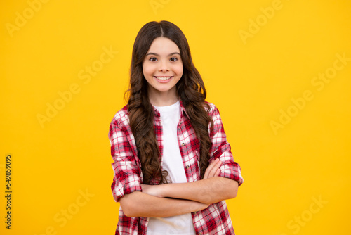 Happy teenager  positive and smiling emotions of teen girl. Teenage girl kid with crossed arms  looking at camera  isolated on yellow studio background.