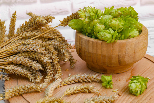 Fresh green hops and ears of wheat on wooden board, closeup