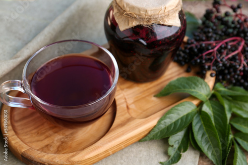 Elderberry jam, glass cup of tea and Sambucus berries on table