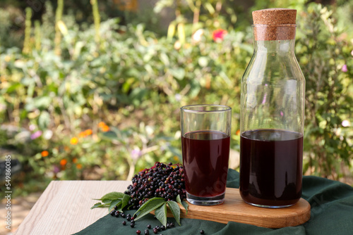Elderberry drink and Sambucus berries on table outdoors, space for text