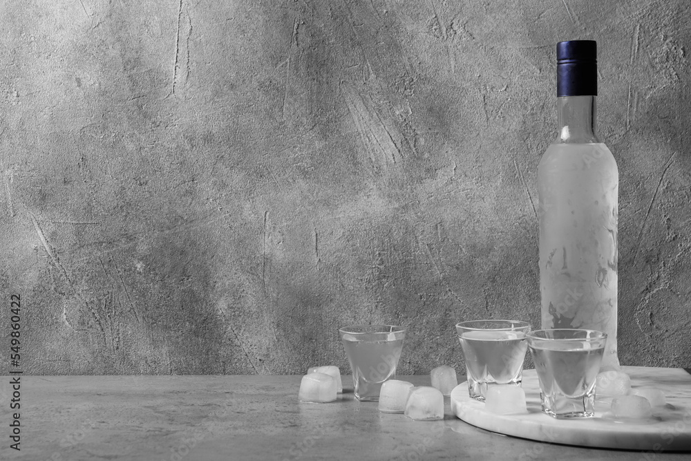 Bottle of vodka and shot glasses with ice cubes on table against grey wall. Space for text - obrazy, fototapety, plakaty 
