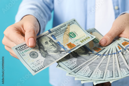 Woman holding dollar banknotes on turquoise background, closeup. Money exchange concept