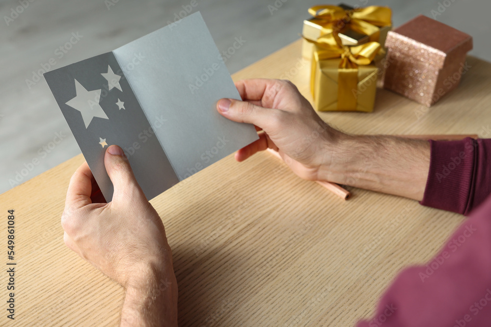 Man holding greeting card at wooden table, closeup Man holding greeting card at wooden table, closeup