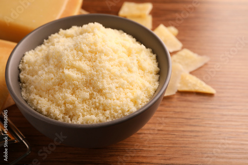 Delicious grated parmesan cheese in bowl on wooden table, closeup