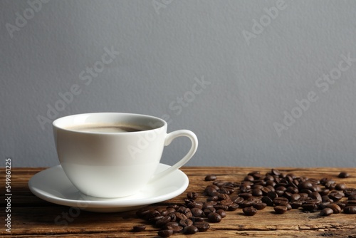 Cup of aromatic coffee and beans on wooden table. Space for text