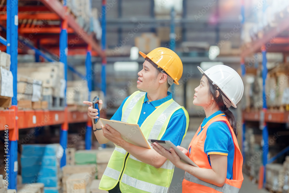 Asian engineer in helmets order and checking goods and supplies on shelves with goods background in warehouse.logistic and business export ,Warehouse worker checking packages on shelf in a large store Asian engineer in helmets order and checking goods and supplies on shelves with goods background in warehouse.logistic and business export ,Warehouse worker checking packages on shelf in a large store