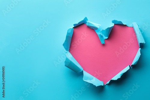Torn heart shaped hole in light blue paper on pink background, space for text