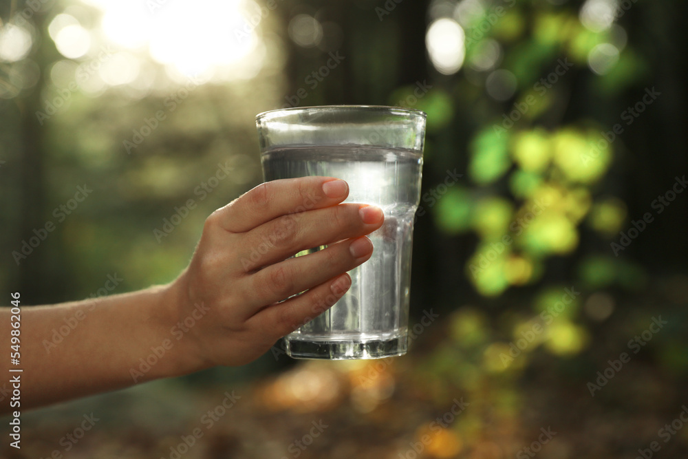 Woman holding glass of fresh water in forest, closeup Woman holding glass of fresh water in forest, closeup