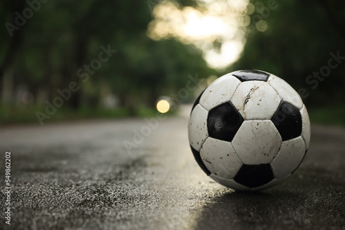 Dirty leather soccer ball on wet road, space for text