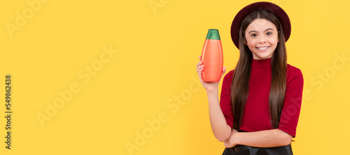 glad kid in hat hold hair conditioner bottle on yellow background  hair condition. Banner of child girl hair care  studio poster header with copy space.