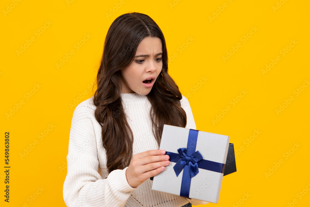 Child with gift present box on isolated background. Presents for birthday, Valentines day, New Year or Christmas. Angry face, upset emotions of teenager girl. Child with gift present box on isolated background. Presents for birthday, Valentines day, New Year or Christmas. Angry face, upset emotions of teenager girl.